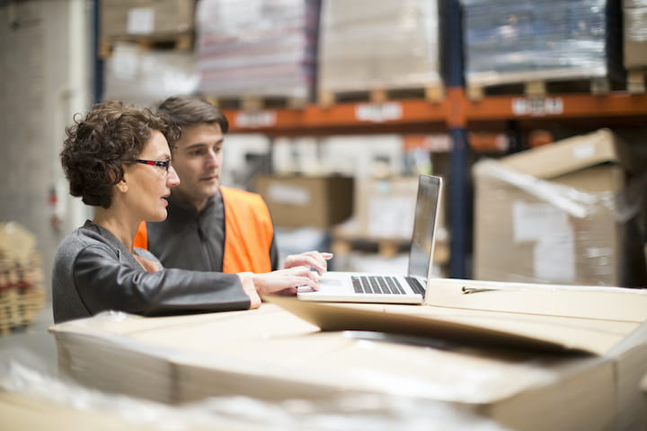 Two people using a laptop in a warehouse