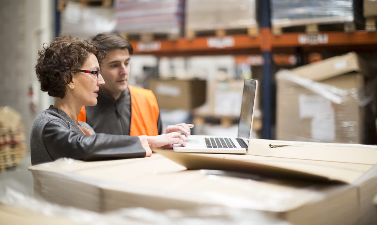 Two people using a laptop in a warehouse